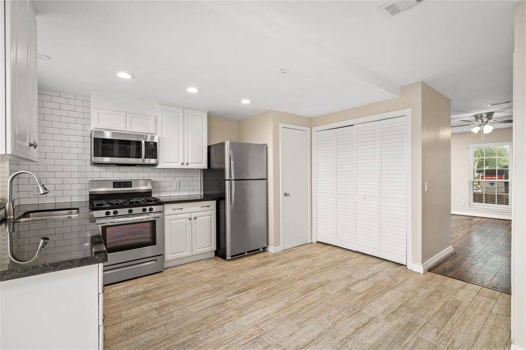 Designed with both aesthetics and efficiency in mind, this area features elegant glass cabinetry, sleek black countertops, and a neutral palette that complements the natural wood-look tile floors. A nearby pantry and utility closet provide added convenience and functionality