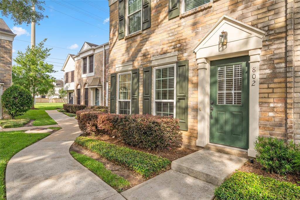 Side view showcases the home’s well-maintained brick exterior and consistent architectural detailing. A neatly trimmed hedge and walkways emphasize the thoughtful landscaping and serene setting within the community.
