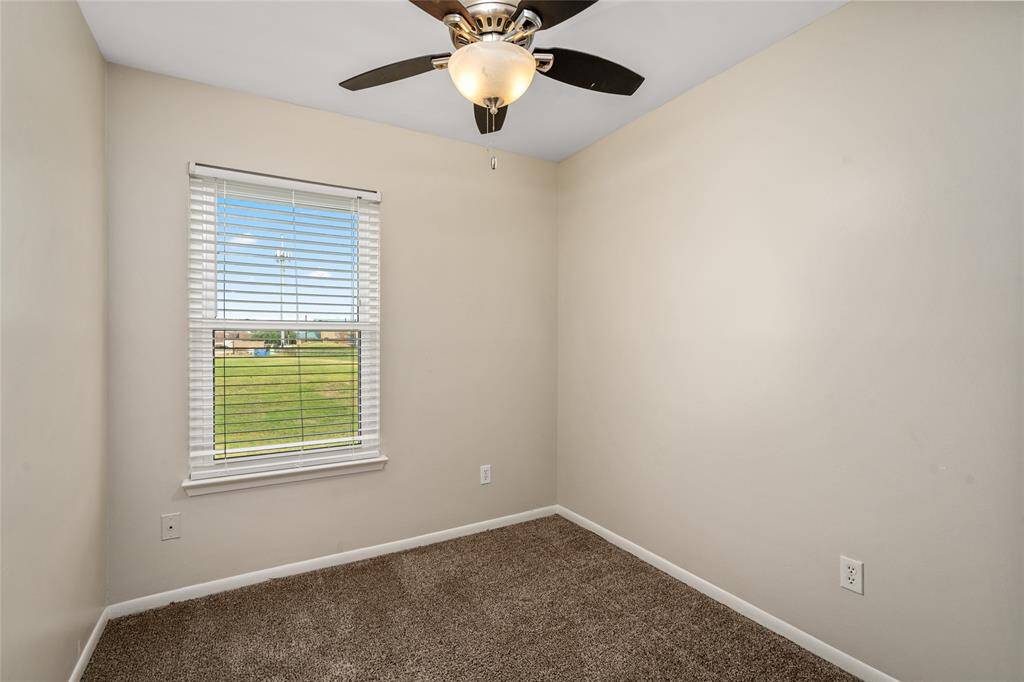 This inviting secondary bedroom offers soft carpet flooring, ample natural light from a wide window, ideal for a guest room, kids’ space, or flexible home office.