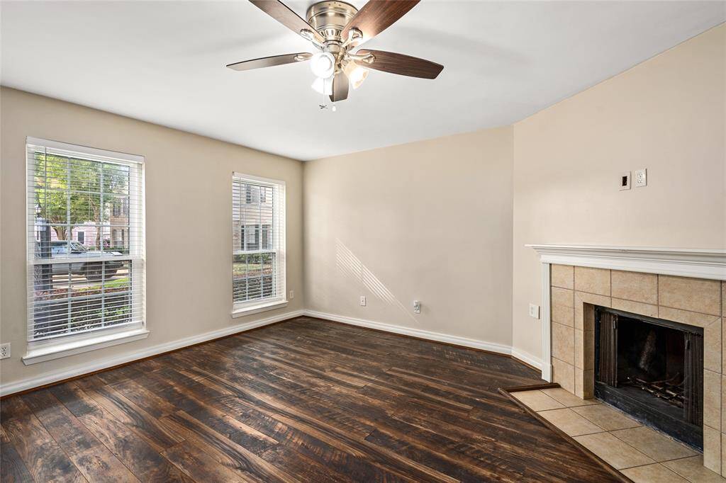 Cozy living space enhanced by a tiled corner fireplace and rich wood-style flooring. Dual windows provide ample natural light, creating a bright and comfortable atmosphere ideal for everyday living.