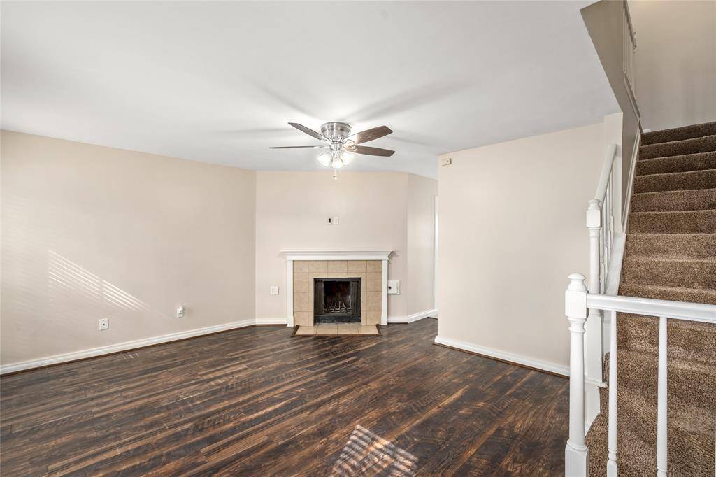 Warm and inviting living area featuring a corner fireplace with tile surround, complemented by dark wood-look flooring and soft natural light from multiple windows. A clean, neutral palette offers a versatile backdrop for any style.