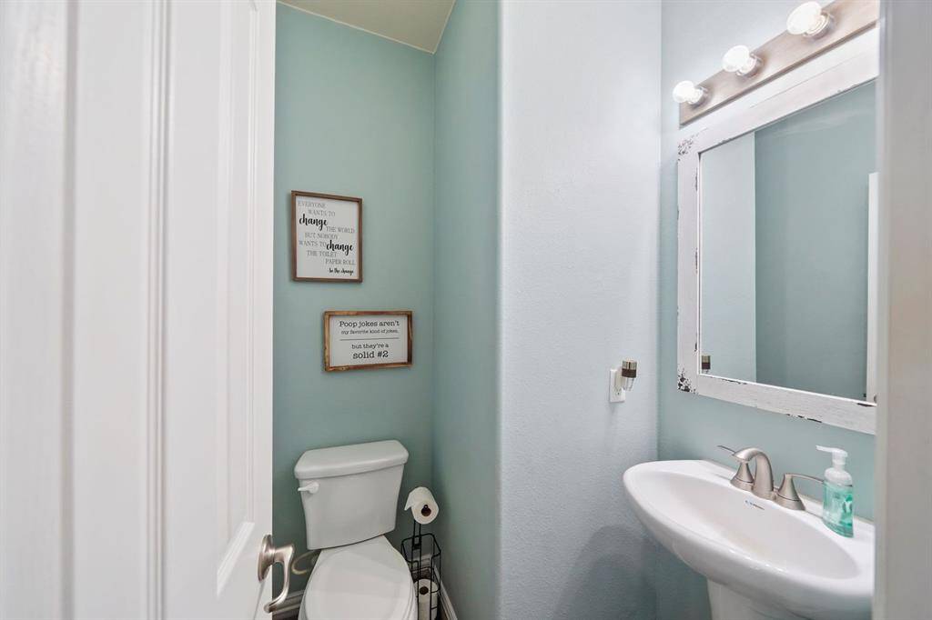 The powder room is the half bath for convenience and for guest. It features a fresh, light blue color scheme, a pedestal sink, and a decorative wall-mounted mirror with overhead lighting adding a touch of personality to the space.