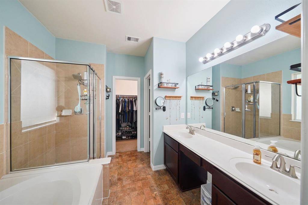 The primary bathroom is designed with a large vanity with two sinks, and a full-sized mirror with bright lighting above.  There is access to a walk-in closet.