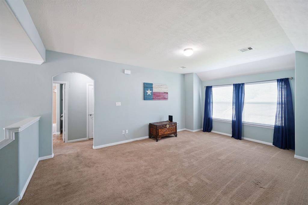 This spacious game room is a well-lit room with neutral walls, vaulted ceiling, and carpeted flooring. It features two large windows and has ample space for customization.