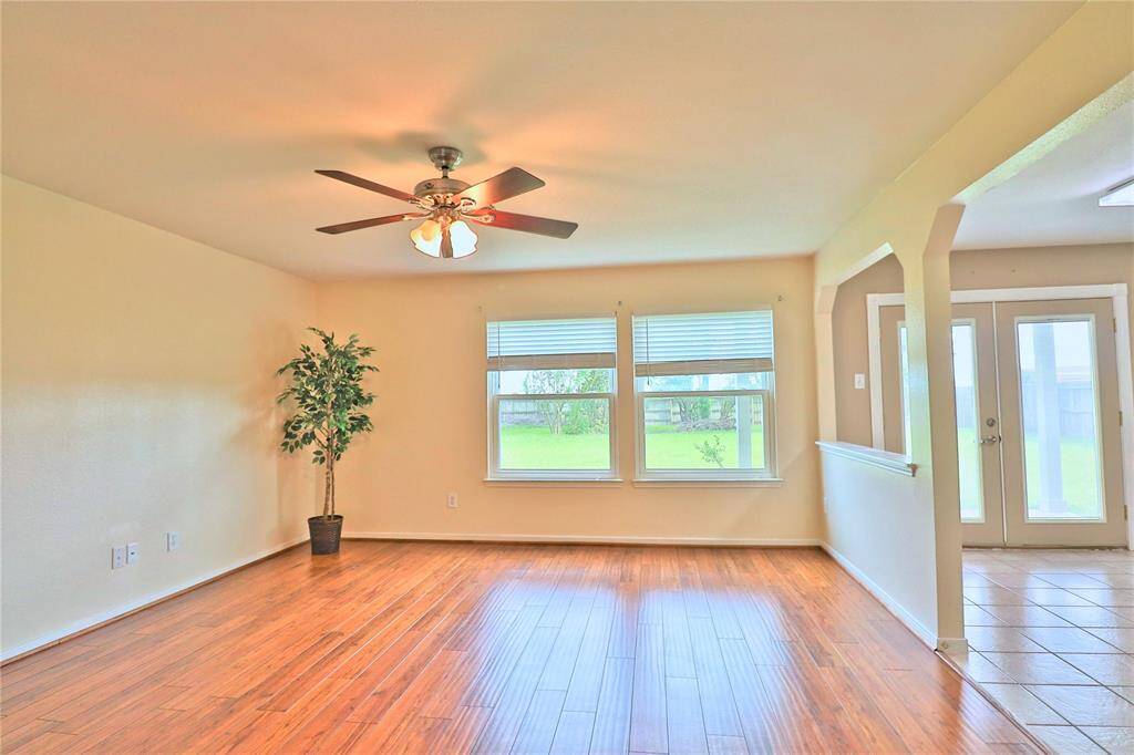 Bright and spacious  family room room with wood flooring, a ceiling fan, large windows offering natural light, and a view of the green backyard.