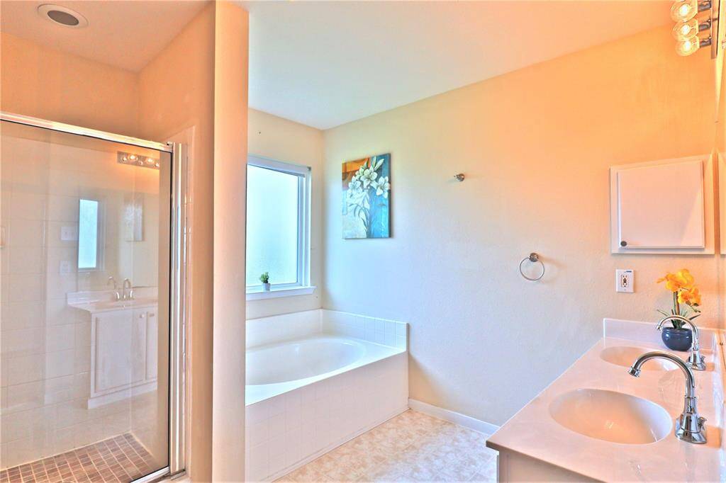 Bright bathroom featuring a spacious tub, separate glass-enclosed shower, dual sinks with a large countertop, and a window allowing natural light.