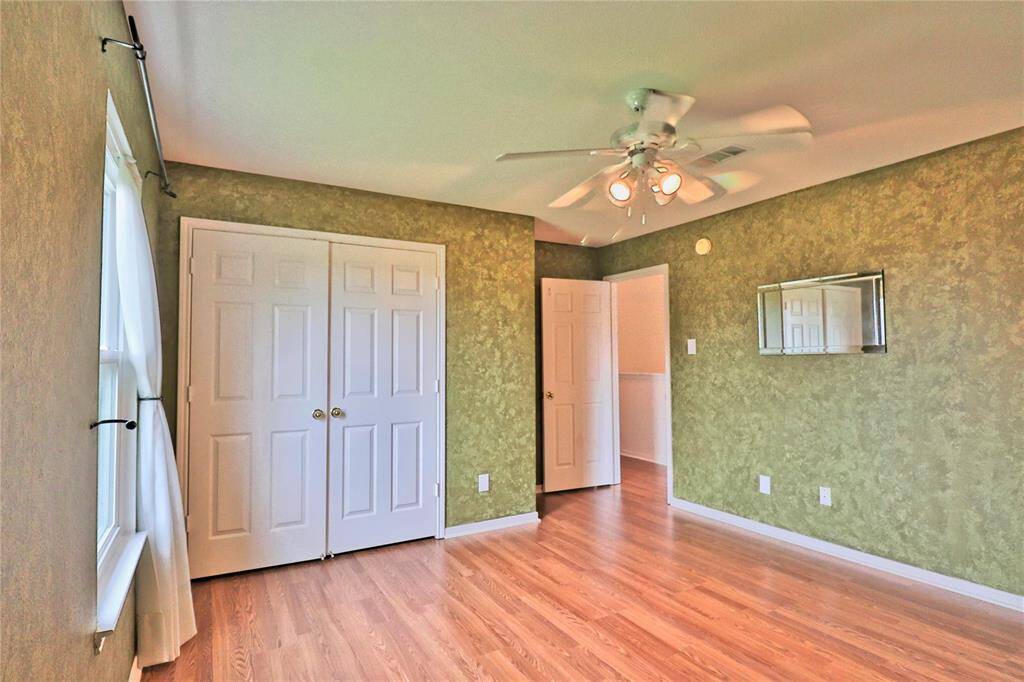 one secondary bedroom 1  features a wood floor, green textured walls, and ample natural light  and a ceiling fan.