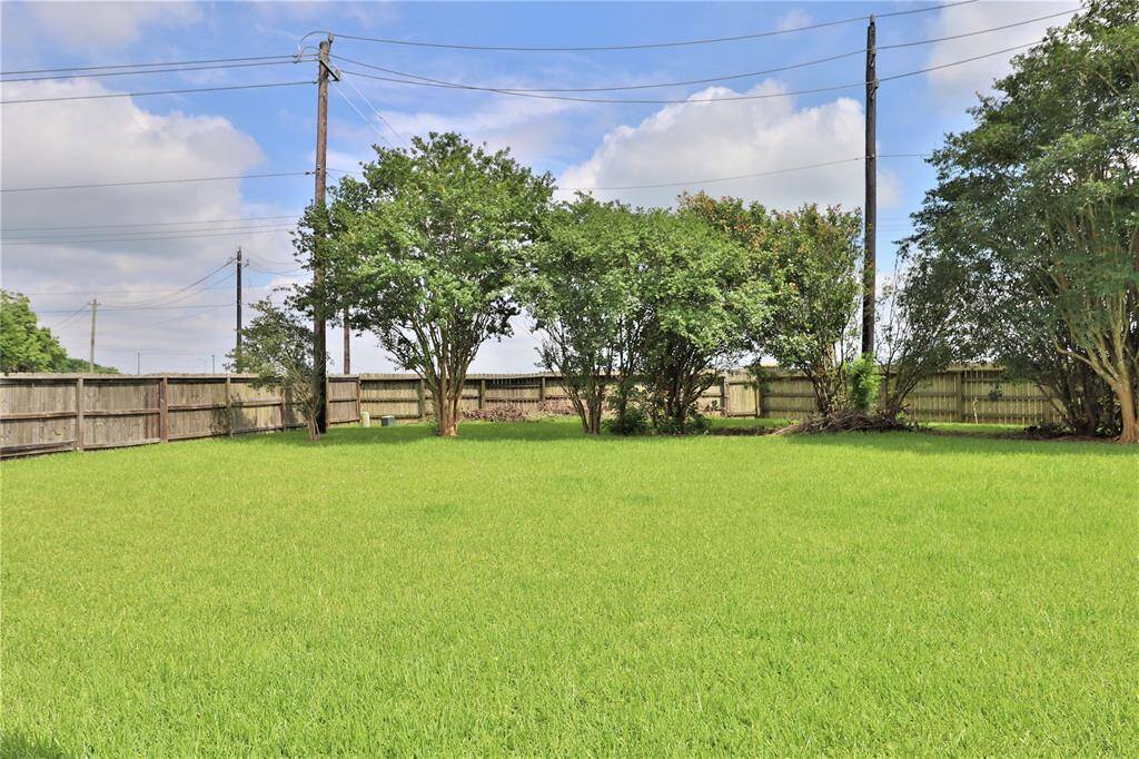 Spacious backyard with lush green lawn, bordered by a wooden fence for privacy. Mature trees provide shade and natural beauty, perfect for outdoor activities or relaxation.