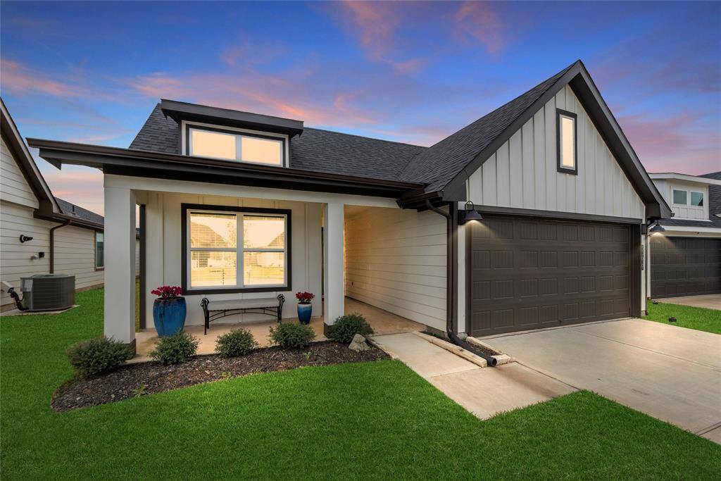 This charming, modern white house features striking black accents that give it a contemporary yet classic feel. A spacious front porch welcomes visitors, offering a cozy outdoor space. The large front window brings in natural light, creating a bright and airy atmosphere inside. Above the garage, a sleek window adds architectural interest, seamlessly blending with the clean lines of the modern design. The cute landscaping surrounding the house includes lush greenery and well-placed plants.