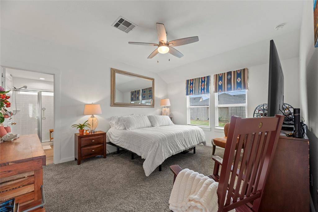 The primary suite is a serene retreat, featuring soft carpet underfoot for added comfort. Two windows bring in natural light, brightening the room and enhancing the airy feel. The light walls create a calm, neutral backdrop, while the ceiling fan ensures a cool, comfortable environment. The suite also includes a connecting bathroom, offering convenience and privacy, making it the perfect space for relaxation.
