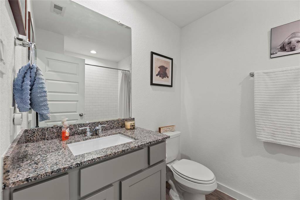 The bathroom features a sleek, modern design with a single vanity topped with beautiful granite countertops. A square, contemporary sink sits above the countertop, paired with a stylish nickel faucet that adds a touch of elegance. The light-colored walls create a fresh, airy feel, complementing the clean lines of the space. Above the sink, a large frameless mirror enhances the openness of the room, reflecting light and creating a bright, spacious atmosphere. This bathroom is both functional and chic.