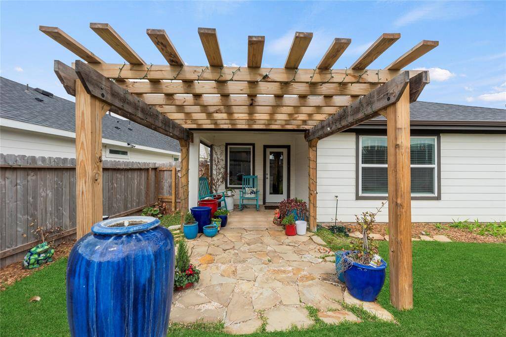 The back of the house features a door that opens up to a charming pergola with a stone patio, offering a perfect space for outdoor relaxation and entertainment. Beyond the patio, a lush green lawn stretches out, fenced in for privacy and security, creating an ideal spot for pets or outdoor activities.