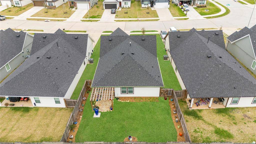 In an aerial view of the backyard, you’ll see a charming pergola framed by rocks, creating a cozy and stylish outdoor space. The pergola sits atop a stone or gravel patio, providing a shaded area for relaxation or dining. Surrounding the patio is a lush green lawn, offering plenty of space for outdoor activities or simple enjoyment of the open air. The edges of the lawn are neatly framed, possibly with rocks or low landscaping elements, adding structure and a natural, polished look to the overall backyard.
