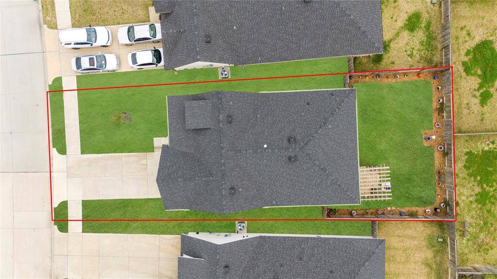 An aerial view of the entire house reveals the modern design, with the white exterior accented by black details, giving it a contemporary and elegant look. The spacious front porch, with the green front door, is a focal point, welcoming visitors. The driveway extends alongside the house, providing ample parking. Around the back, the pergola and stone patio are clearly visible. The overall layout of the home showcases its seamless integration with the outdoor spaces, providing a harmonious flow.