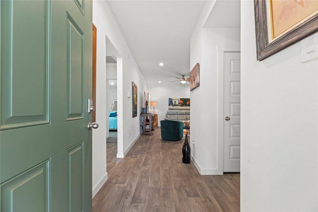 The green front door opens to a bright, welcoming interior featuring LVP flooring in a natural wood color, which adds warmth and character to the space. The white walls create a clean, modern backdrop, while sleek, modern baseboards add a touch of refinement. Straight ahead, the hallway leads into the living room, offering an inviting space for relaxation and socializing.