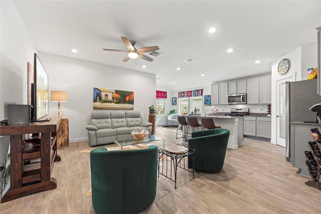 The living room is spacious and inviting, seamlessly opening up to the kitchen for a bright, open-concept feel. Recessed lighting in the ceiling provides ample illumination, while a ceiling fan adds comfort and circulation. With plenty of space for furniture, the room offers flexibility in arranging seating to suit your style. The natural LVP floors add warmth and a touch of modern charm, tying the space together beautifully. It's an ideal spot for relaxation, socializing, and family gatherings.