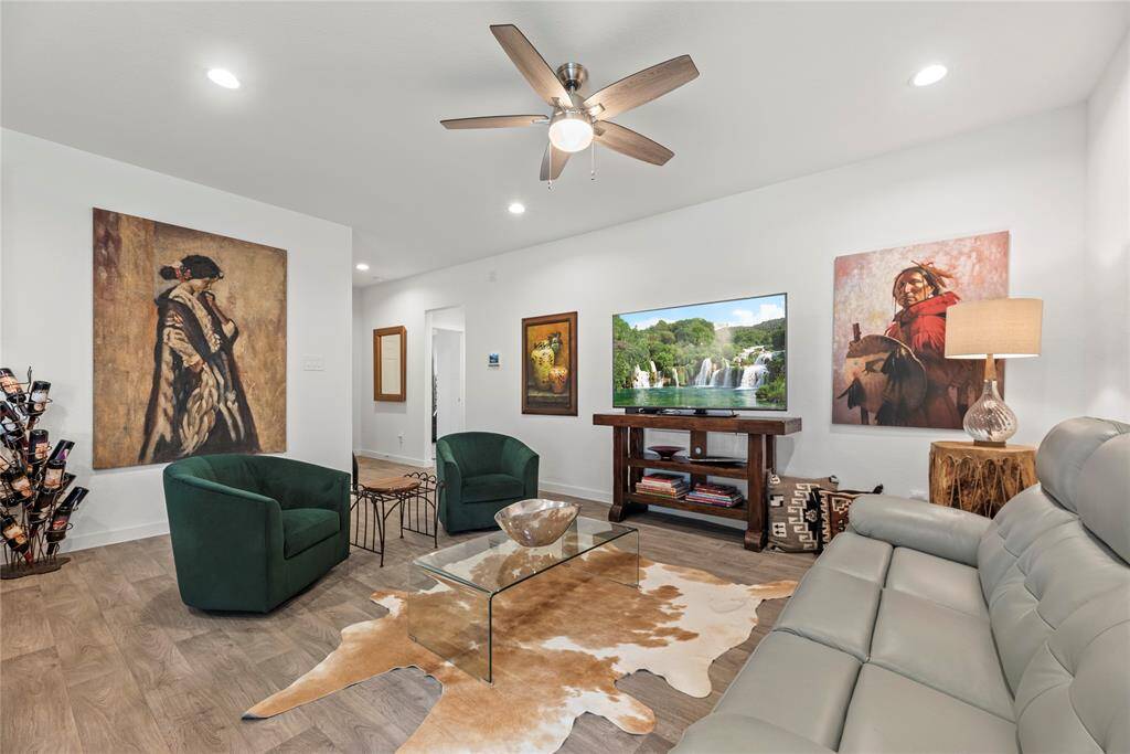 From this different angle, the living room reveals the hallway leading to the other rooms, offering a seamless flow throughout the home. The spacious layout still shines, with plenty of room for furniture and an open connection to the kitchen. The recessed lighting and ceiling fan continue to provide both ambiance and comfort, while the natural LVP floors run throughout, maintaining a consistent, warm feel across the space.
