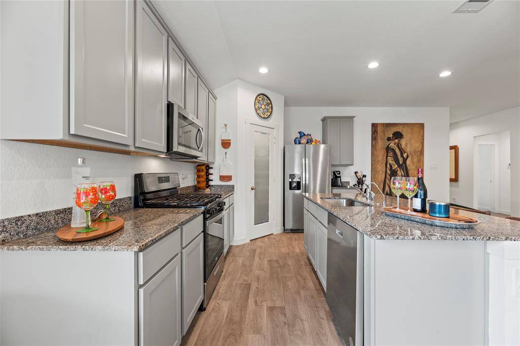 The kitchen is equipped with sleek stainless steel appliances, adding a polished, modern touch. A corner pantry provides ample storage space, making it easy to keep everything organized. The sink is conveniently located on the island, offering both functionality and a central gathering spot for meal prep or casual conversation. With gray cabinets, granite countertops, and these thoughtful features, the kitchen is both stylish and highly functional, perfect for cooking and entertaining.
