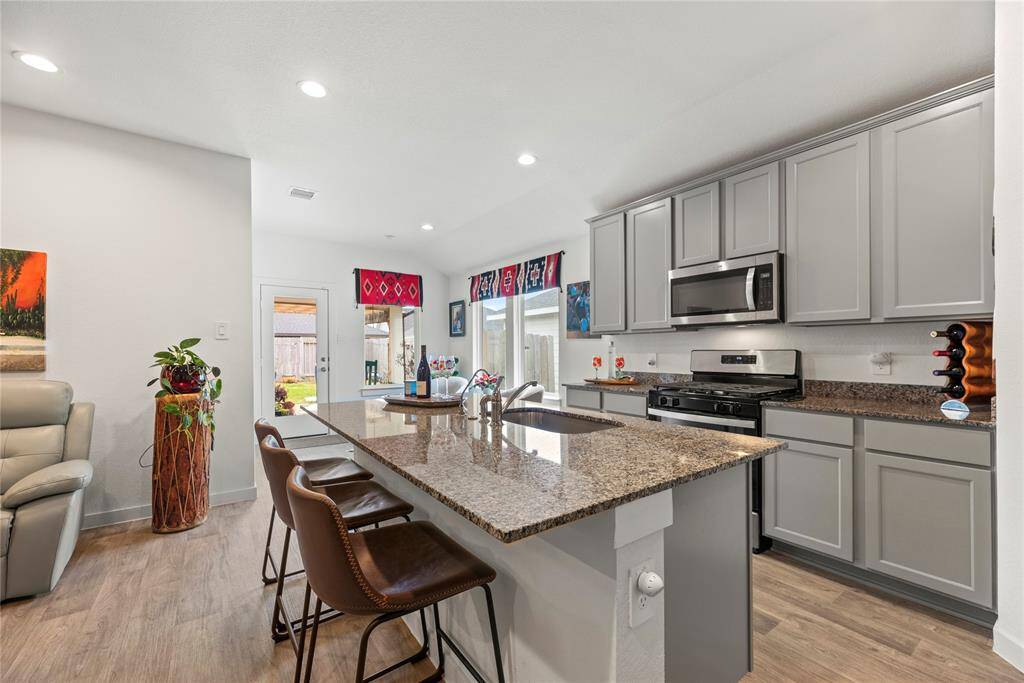The kitchen features stylish gray cabinets that contrast beautifully with the sleek granite countertops, creating a modern and sophisticated look. A cozy breakfast area is situated by surrounding windows, allowing for plenty of natural light and offering a pleasant spot for casual meals. The back door conveniently leads to the back patio, providing easy access to outdoor dining or relaxation. This kitchen is both functional and inviting, with a layout that seamlessly connects the indoor and outdoor spaces.