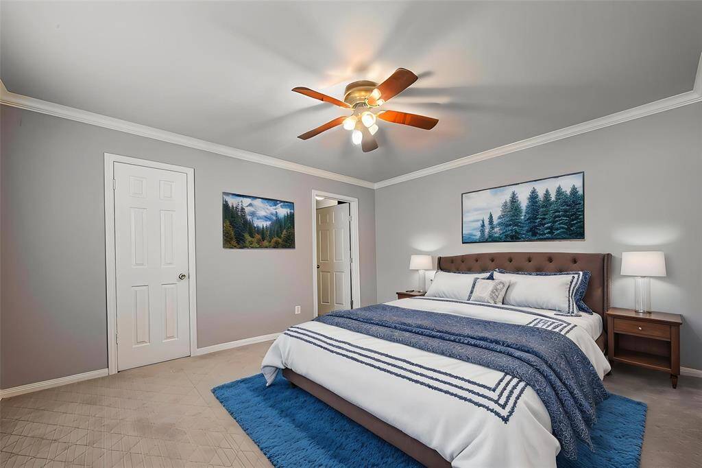 Virtual Staging - This photo shows a cozy bedroom with soft gray walls and a ceiling fan. It features a comfortable bed with blue and white bedding, two nightstands with lamps, and decorative wall art. The room has a carpeted floor and a small plant, creating a welcoming atmosphere.