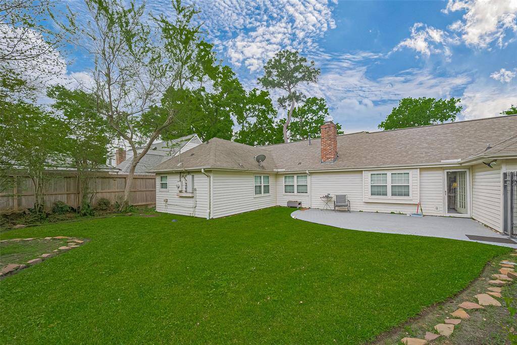 This charming home features a spacious, well-maintained backyard with lush green grass and mature trees. The exterior is inviting, with light-colored siding and ample windows for natural light. A cozy patio area offers space for outdoor relaxation. Perfect for enjoying sunny days.