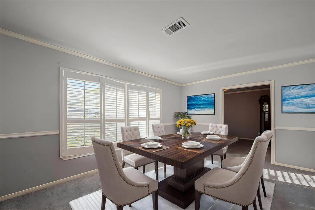 Virtual Staging - Bright dining room with ample natural light from large windows with shutters. Features a stylish wooden table, six upholstered chairs, and modern wall art. Neutral tones enhance the spacious feel.