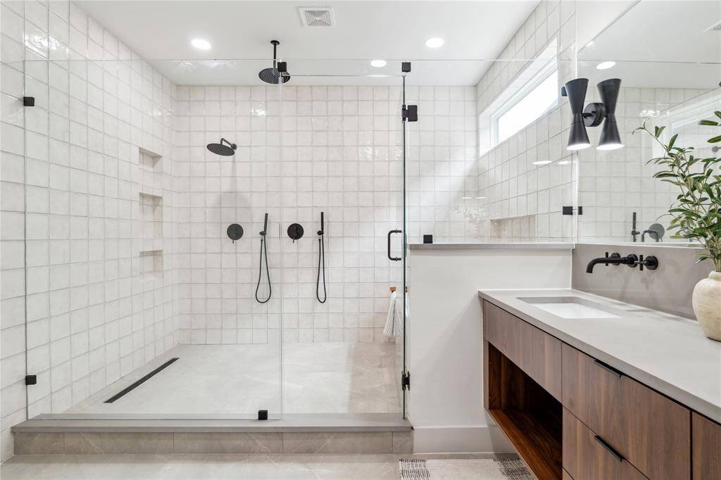 This oversized walk-in shower delivers a spa-worthy experience with dual rain heads, hand showers, and built-in niches—all enclosed in seamless glass to let the custom tile shine.