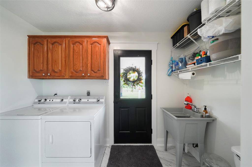 Spacious laundry room with upper cabinets, a utility sink, and backyard access—perfect for muddy boots or quick cleanup after outdoor fun.