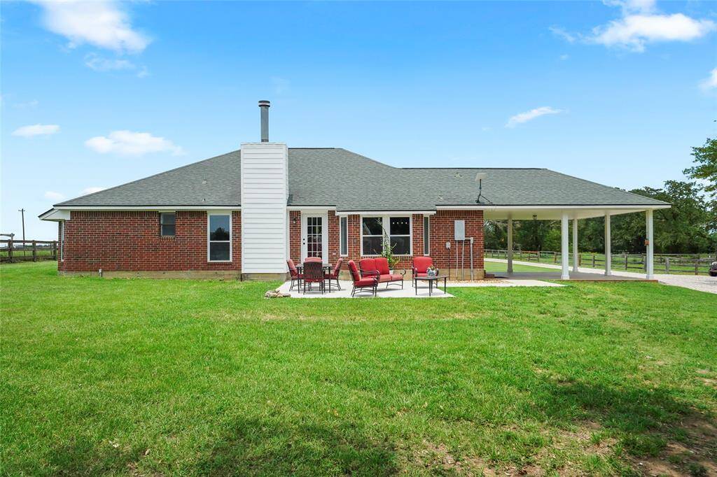 This clean, classic view of the back of the home shows off the brick exterior, covered carport, and wide-open green space.