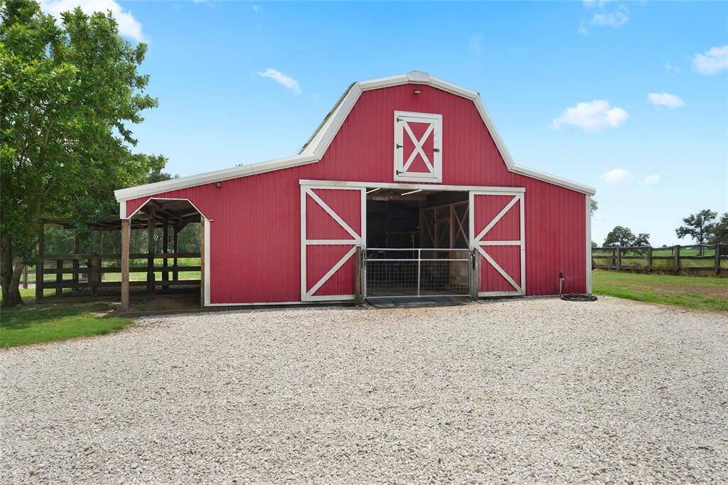 The classic red barn with a large gravel drive offers functional space for animal care, equipment storage, or hobbies. The open-ended design provides excellent airflow and accessibility.