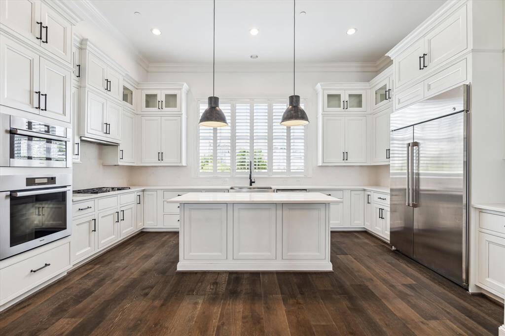 This phenomenal kitchen features a full wall of soft-close Shiloh kitchen cabinets and drawers with endless storage space, glass upper cabinets for display and one section of glass cabinets for glassware. Custom-selected Quartz countertops and backsplash. Large kitchen island with modern light pendants, additional storage with seating/dining space for three.