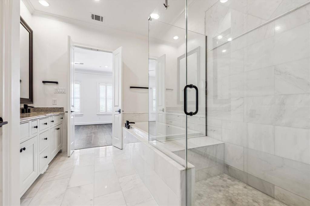 Luxurious primary bathroom features marble tile floors and bath/shower surround, granite countertops, large oversized framed bathroom mirrors, jetted tub and separate shower with frameless glass shower surround,Double Vanity.