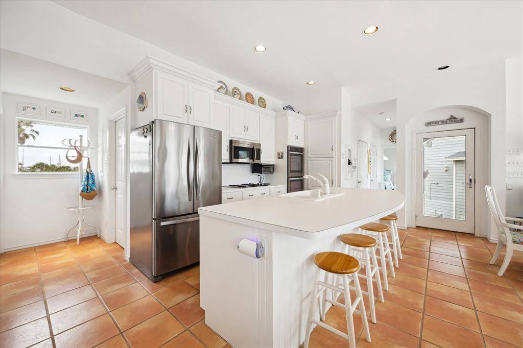 View of the large light filled  kitchen area featuring large island with additional counter seating,stainless steel appliances, freestanding icemaker and plenty of storage cabinets.