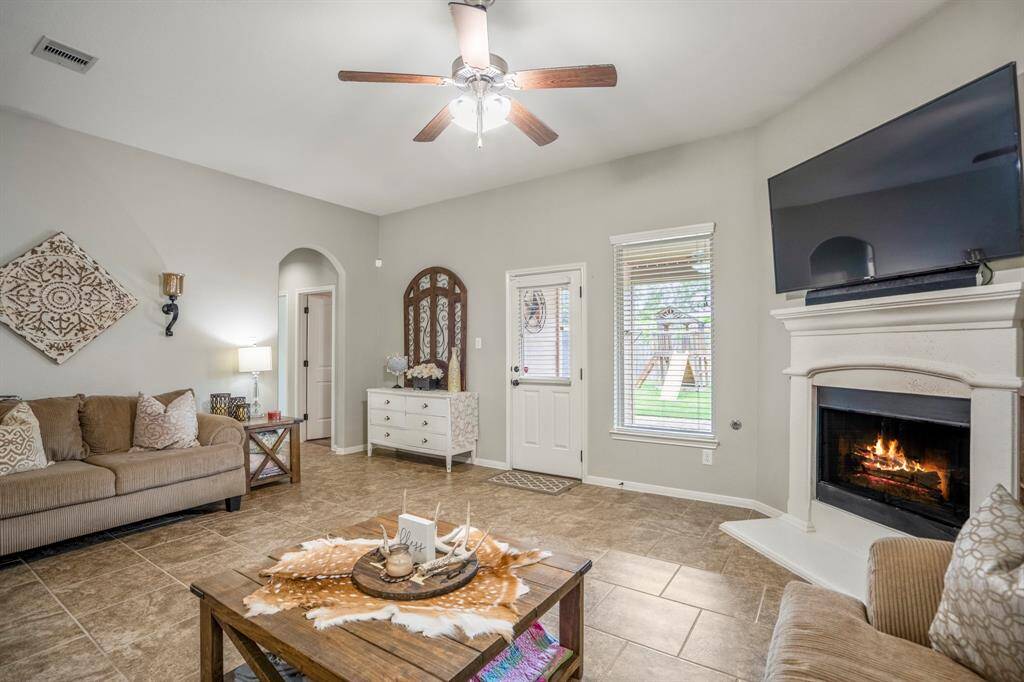 Cozy up in the living room with views of the backyard and a warm corner fireplace. To the left, an arched hallway leads to the spacious primary suite and a nearby bedroom.