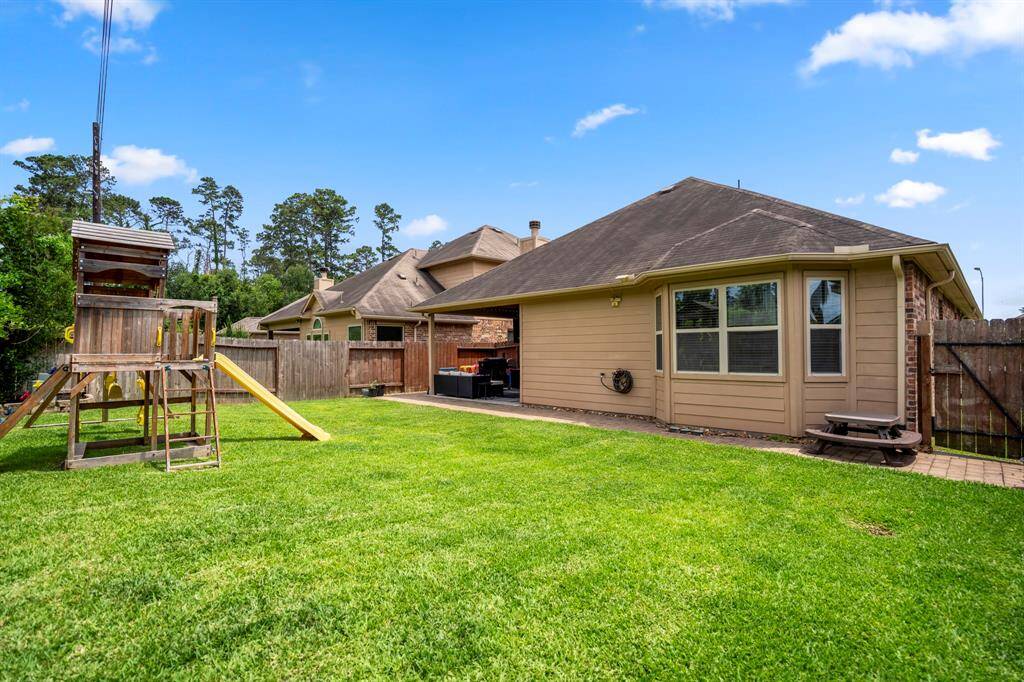 From the back corner of the yard, take in a welcoming view back toward the house—where the covered patio and warm wood ceiling invite you to step inside or linger outside in comfort.