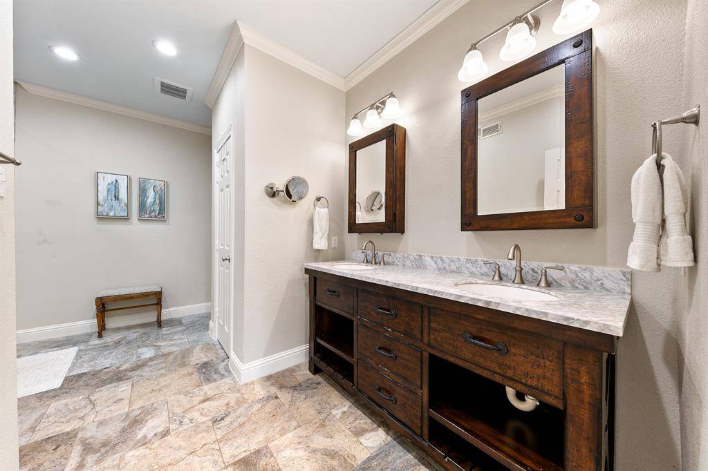The primary bath showcases exquisite hardwood cabinetry and matching framed medicine cabinets, adding a touch of warmth to the space. Dual vanities with marble countertops and undermount sinks are complemented by stunning porcelain tile flooring, creating a serene, spa-like atmosphere that blends both comfort and luxury.
