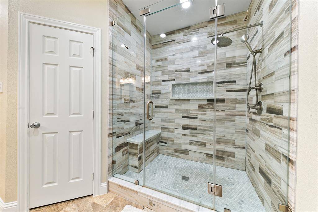The primary bathroom's stunning shower features a seamless glass door, floor-to-ceiling marble tiles, an oversized rain shower head with European wand, a vanity niche, and a built-in bench.  This space is the perfect sanctuary for ultimate relaxation, whether starting or ending your day.