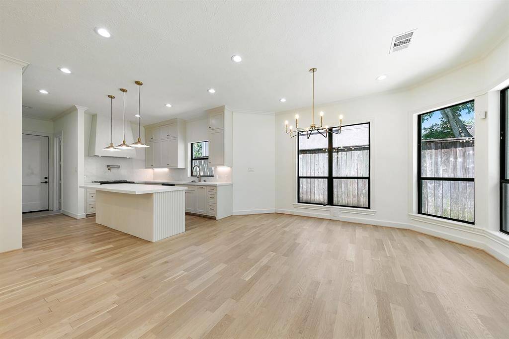 This photo showcases a bright, open-concept kitchen and dining area with hardwood floors, modern light fixtures, and large windows providing ample natural light. The kitchen features a central island with pendant lighting and sleek cabinetry.