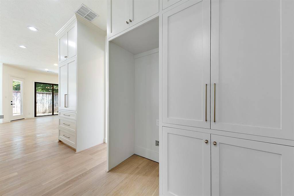 This photo showcases a bright, open-concept space with light hardwood floors, white cabinetry, and ample natural light streaming through a large glass door leading to a fenced backyard. Perfect for modern living.