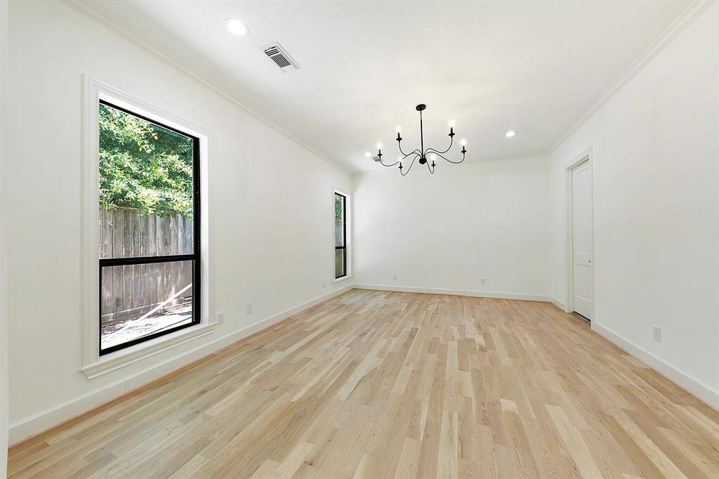 Bright, spacious room with light wood flooring and large windows allowing natural light. Features a modern chandelier and neutral walls, creating a versatile space.