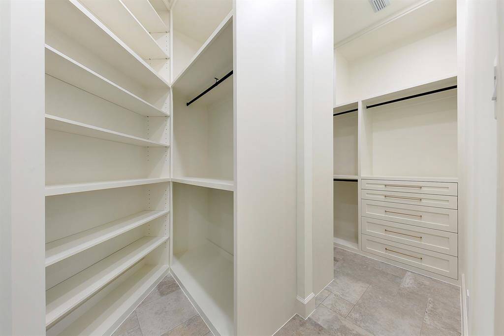This is a spacious, walk-in closet featuring ample shelving, hanging rods, and drawers, perfect for organized storage. The neutral color scheme and tiled flooring add a modern touch.