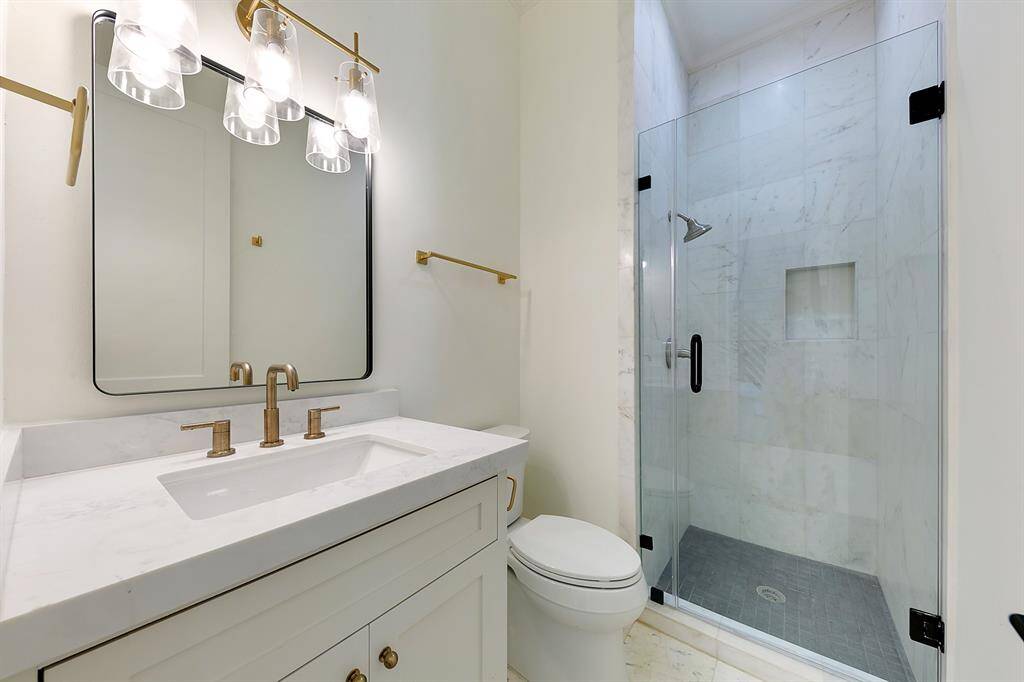 This modern bathroom features a sleek glass-enclosed shower, elegant marble countertops, and stylish gold fixtures, providing a luxurious and contemporary feel.