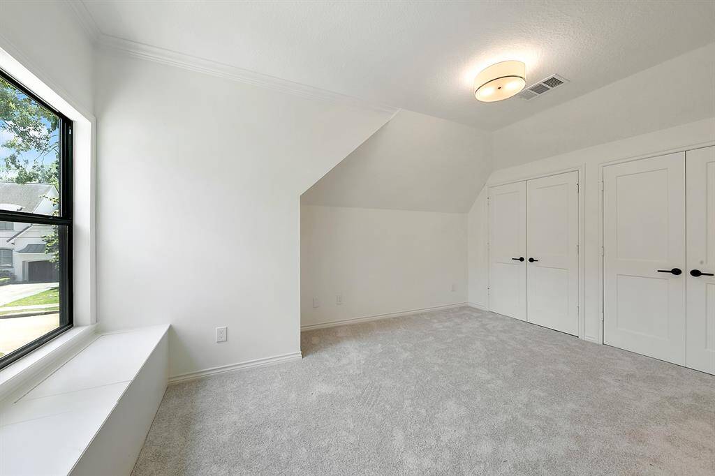 Bright room with soft carpet and neutral walls, featuring a large window seat and double doors. Ideal for a bedroom or office space.