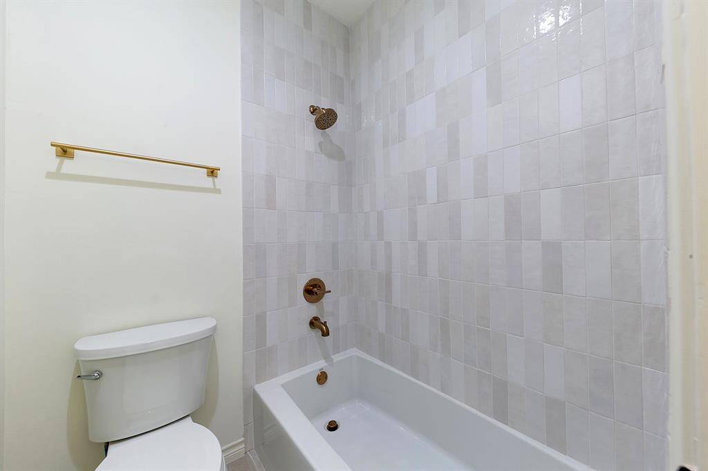 This bathroom features a modern design with light-colored tiled walls, a bathtub-shower combo, and gold fixtures, creating a clean and stylish look.