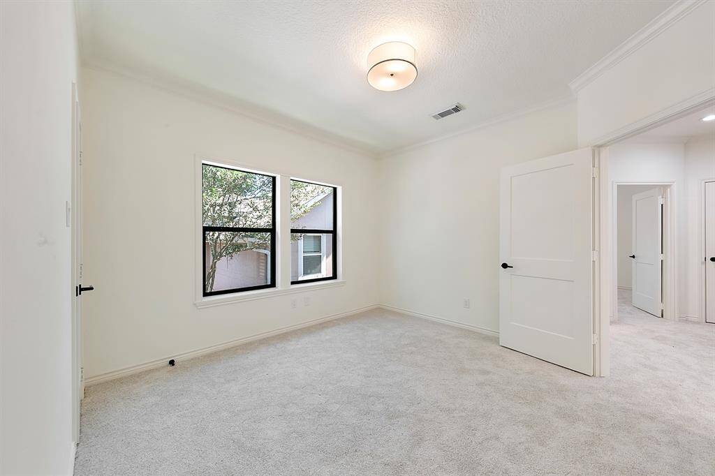 Bright and airy room with soft carpet, a large window for natural light, and a modern ceiling light. Neutral walls and open doorway lead to additional space, perfect for a bedroom or home office.
