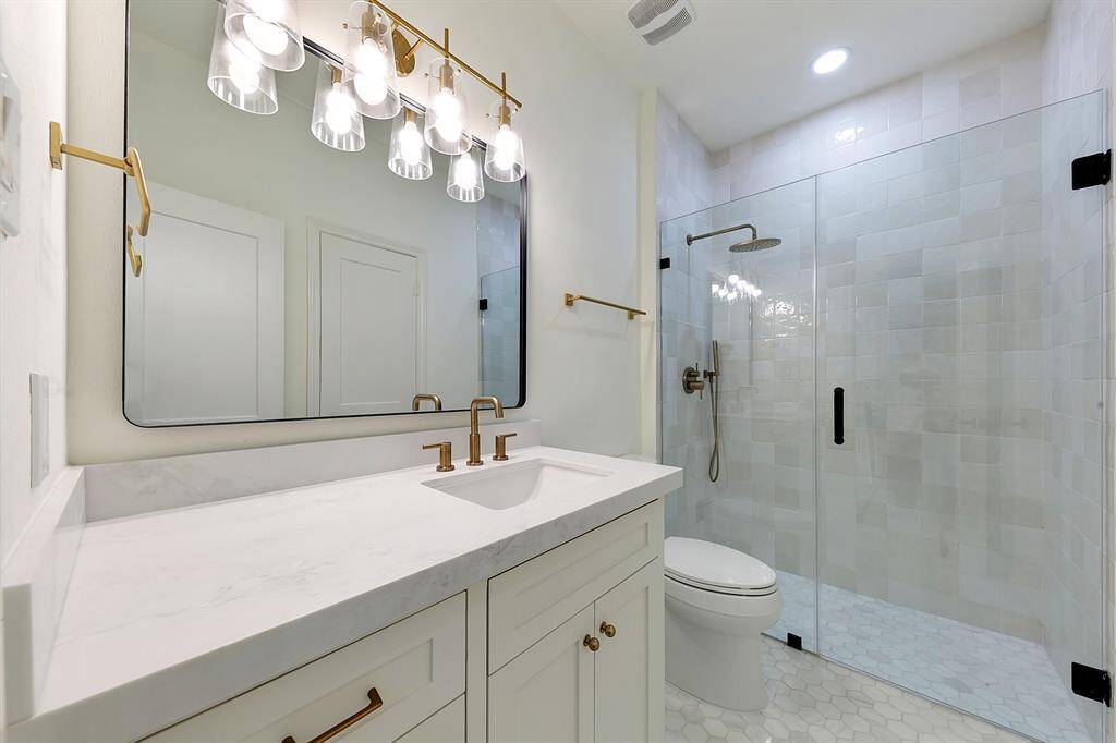 This modern bathroom features a spacious glass-enclosed shower, a sleek vanity with a large mirror, stylish lighting, and elegant brass fixtures. The neutral color palette and clean design create a fresh, inviting atmosphere.