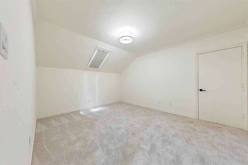 This room is a bright, carpeted space with a sloped ceiling and a modern light fixture. It features a small window for natural light and a simple door, ideal for a bedroom or office.