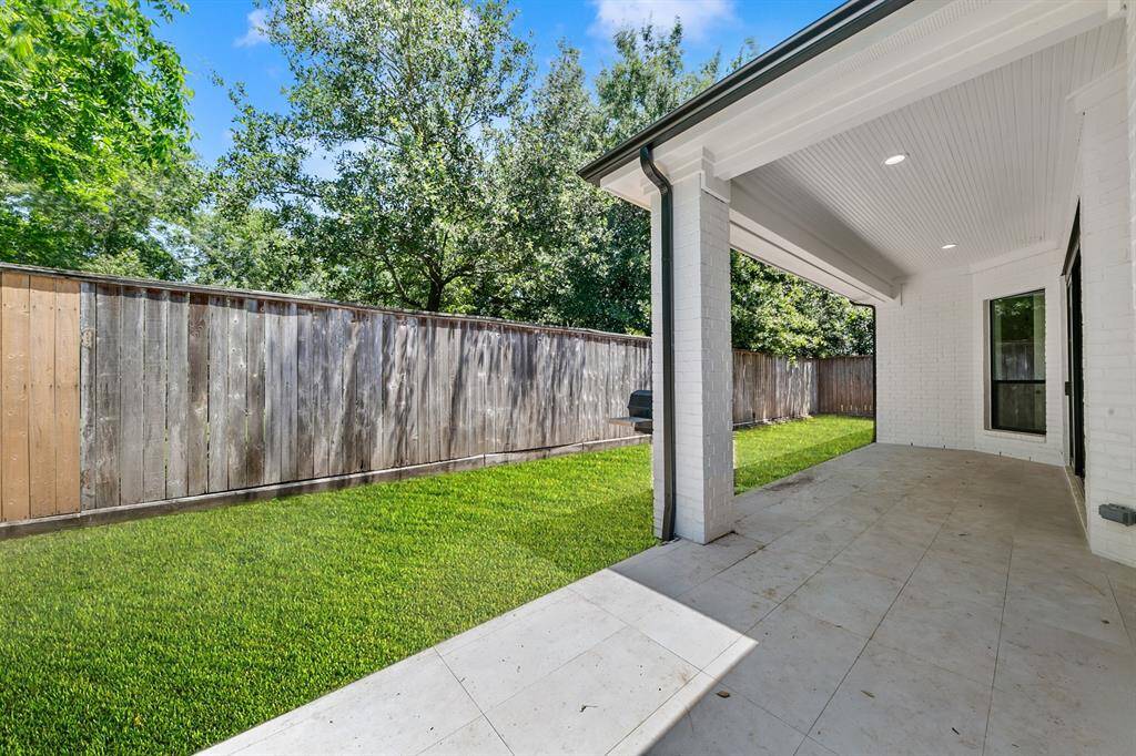 This photo showcases a spacious, covered patio area with a tiled floor, leading to a well-maintained grassy backyard. It features a wooden privacy fence and mature trees, offering a serene and private outdoor space.