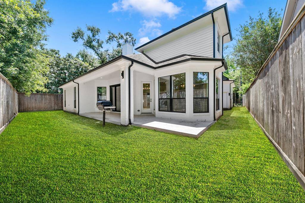 This photo showcases a modern backyard with a well-maintained lawn, a cozy covered patio, and a grill area. The house features large windows and a white exterior, offering a private and inviting outdoor space.