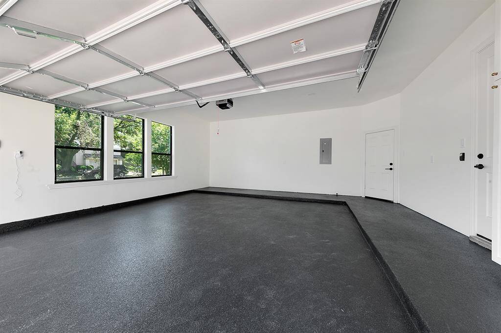 This photo features a spacious, clean garage with a sleek, dark floor and large windows offering natural light. The white walls and ceiling enhance the brightness, and there's a door for easy access to the interior of the home.